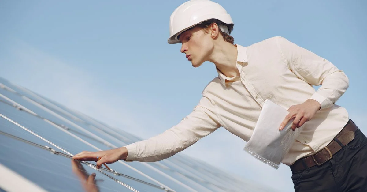 Un technicien solaire en casque inspecte des panneaux photovoltaïques sous un ciel dégagé.