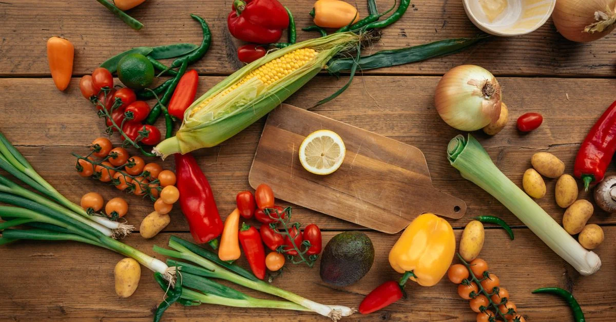 Assortiment coloré de légumes et fruits frais disposés sur une table en bois avec une planche à découper.