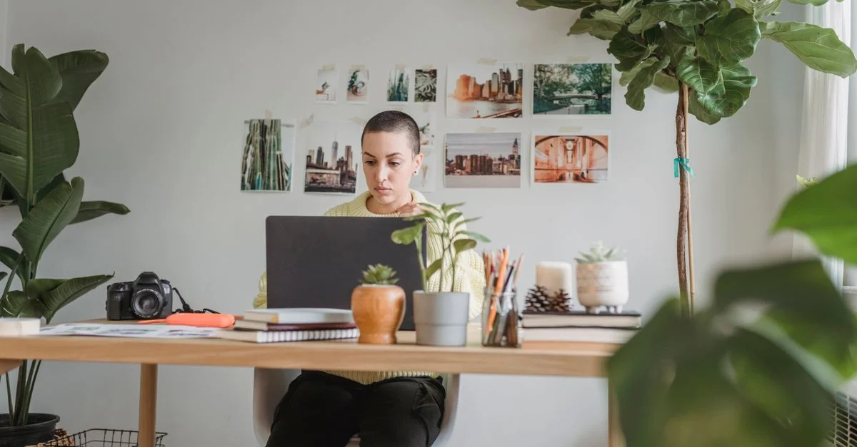 Une femme se concentrant sur son travail à son bureau entourée de plantes et d'équipement photographique.