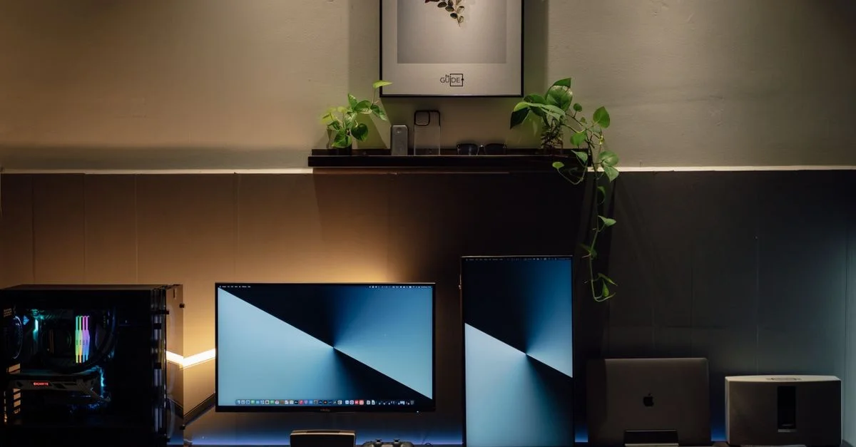 Un bureau moderne avec des écrans doubles, des plantes en pot et des gadgets technologiques.