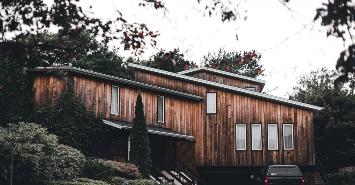 Extérieur moderne et élégant d'une maison en bois avec verdure et une voiture noire garée.