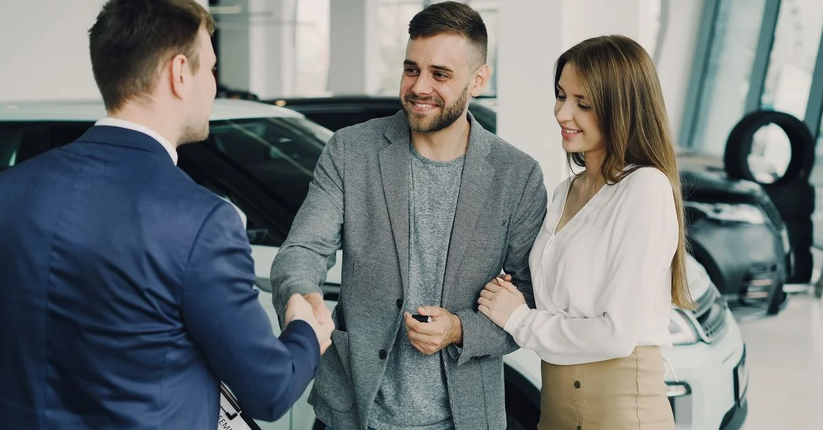 Un couple heureux finalisant l'achat d'une voiture avec un vendeur dans le showroom de la concession. Environnement lumineux et accueillant.