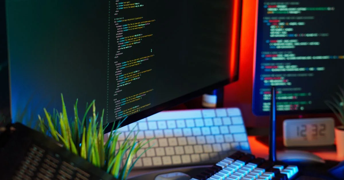 Un espace de travail dynamique présentant des écrans d'ordinateur avec du code, un clavier et des accessoires technologiques.